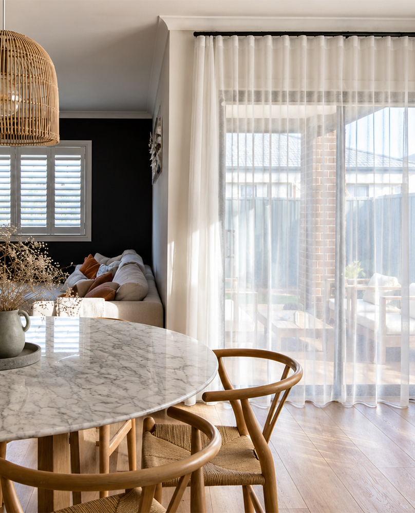 Decorquip white sheer curtains hanging from a black curtain track across patio doors in a modern dining and living area