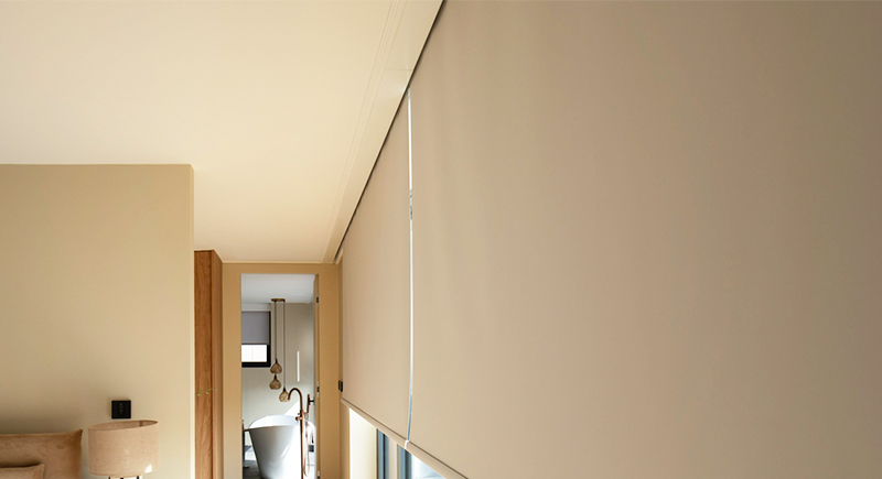 Decorquip beige roller blinds in Blindspace lowered over tall bedroom windows