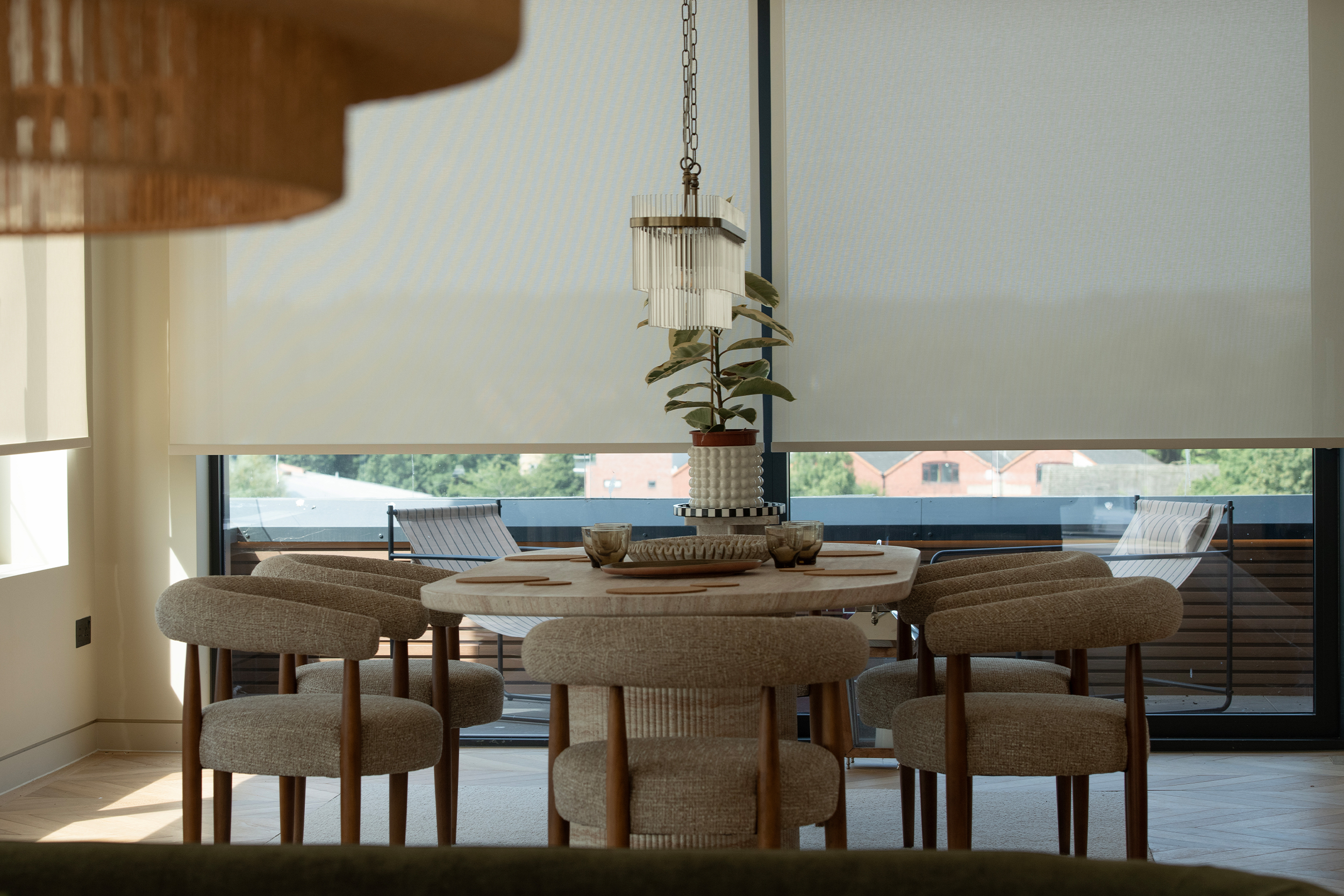Decorquip cream roller blinds partially lowered over wide windows behind a dining table
