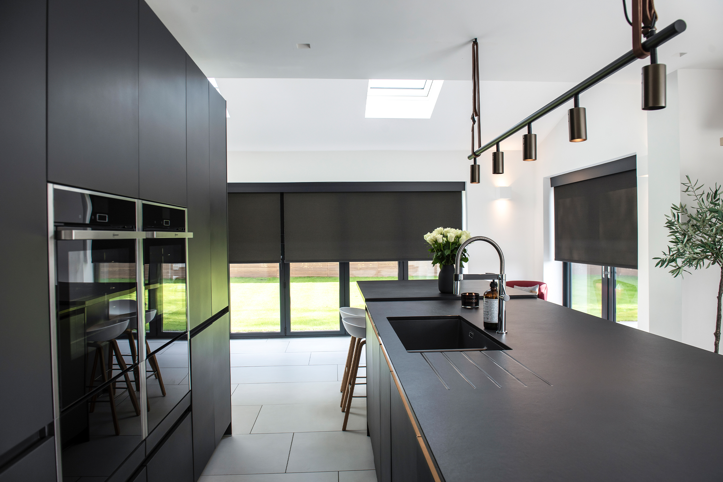 Decorquip dark grey roller blinds partially lowered over large windows in a modern kitchen