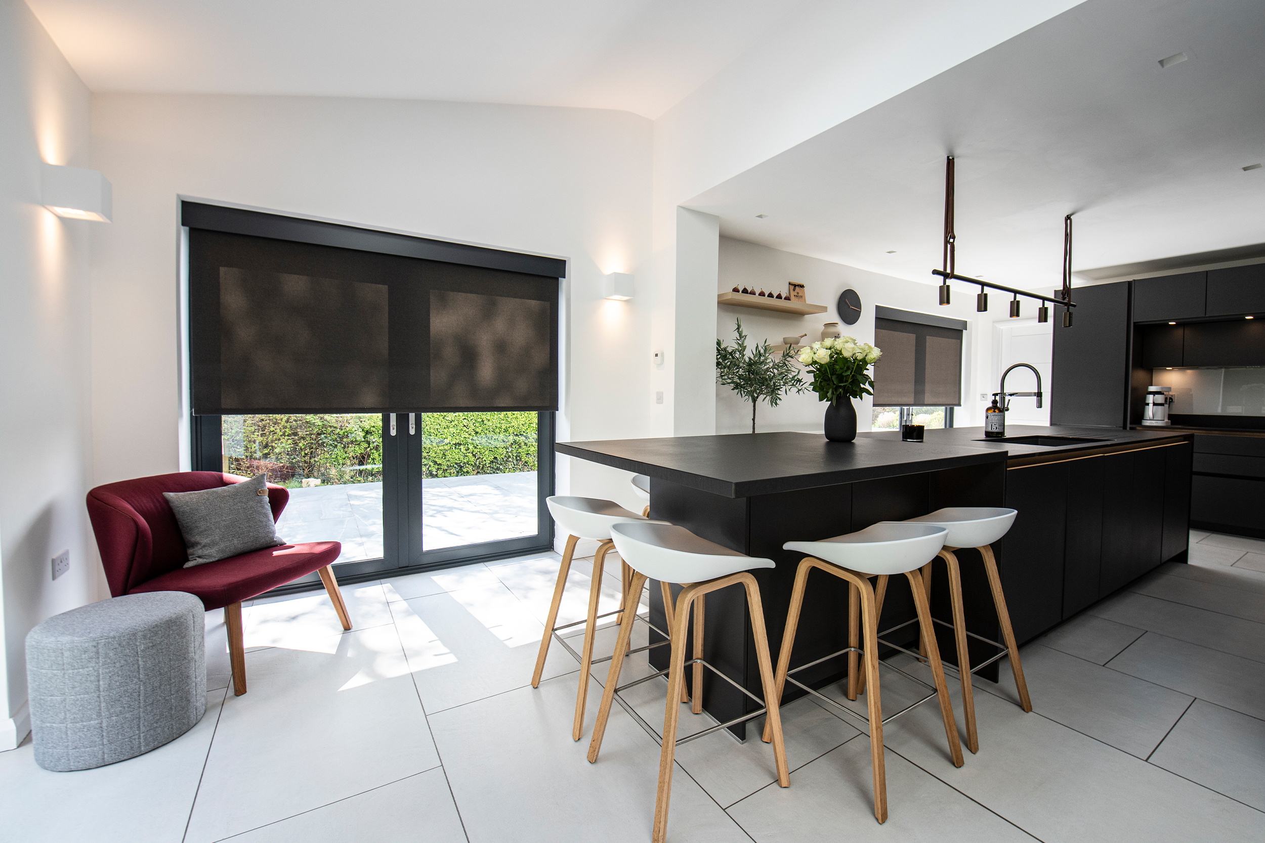 Decorquip dark grey roller blinds partially lowered over large windows in a modern kitchen