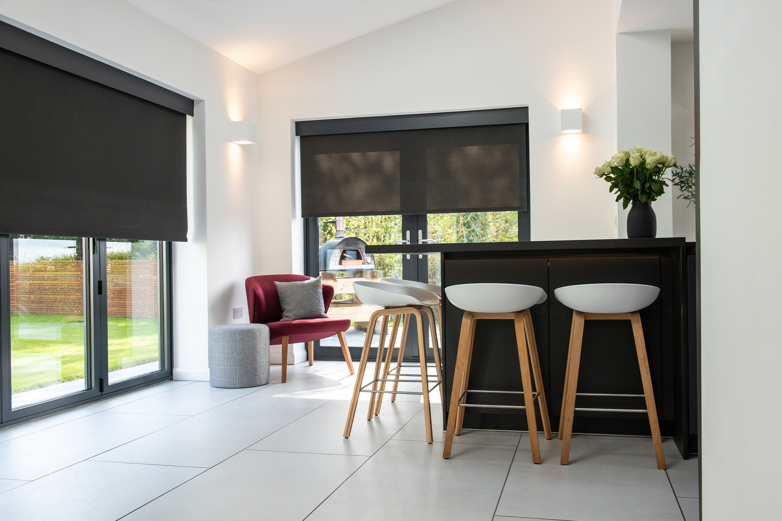 Decorquip dark grey roller blinds partially lowered over large windows in a modern kitchen