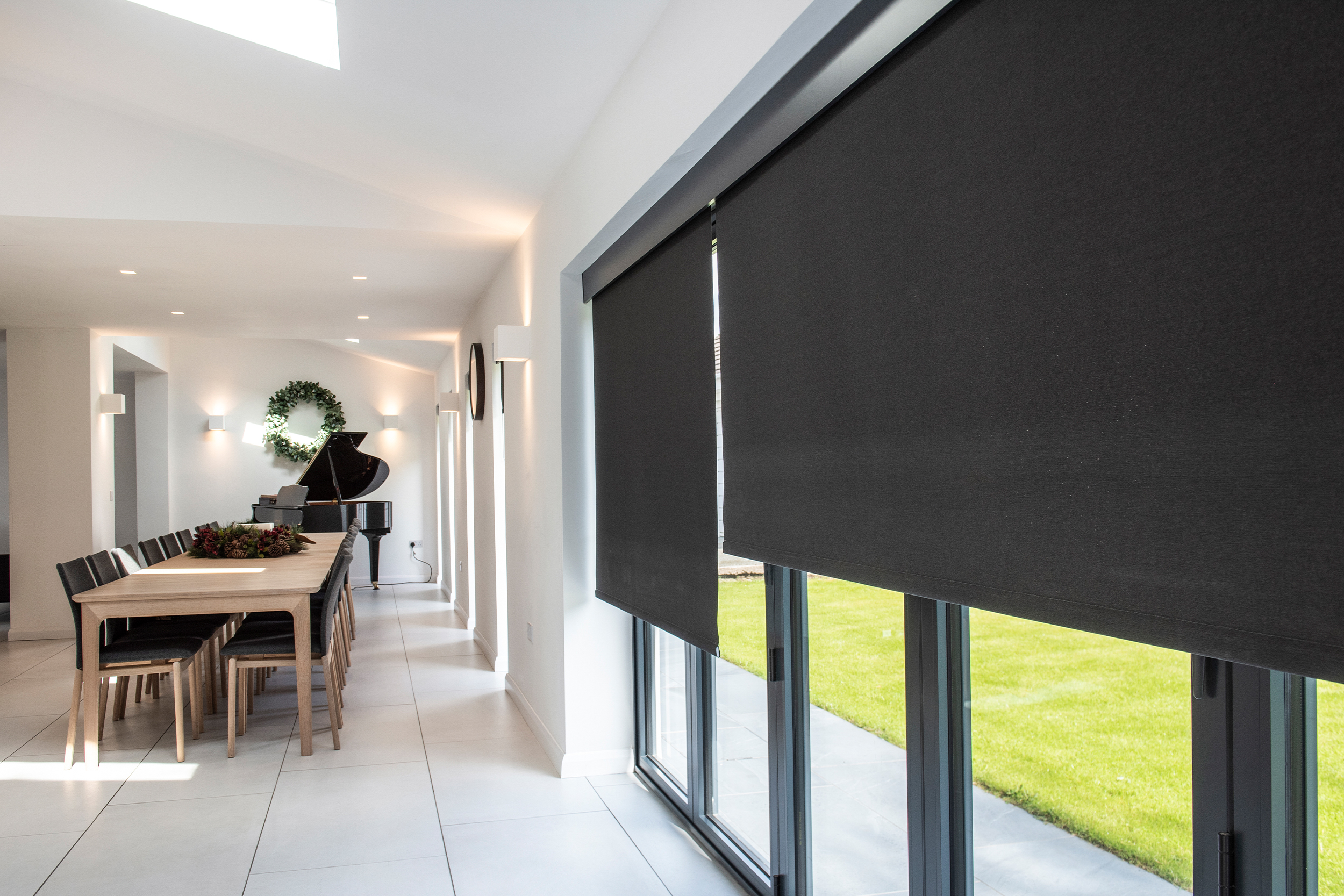 Decorquip dark grey roller blinds partially lowered over large windows in a modern kitchen