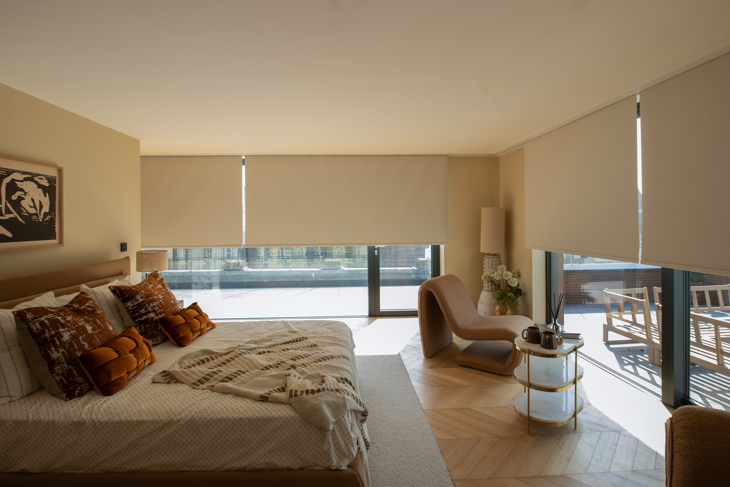 Decorquip cream roller blinds partially lowered over floor-to-ceiling windows in a neutral bedroom