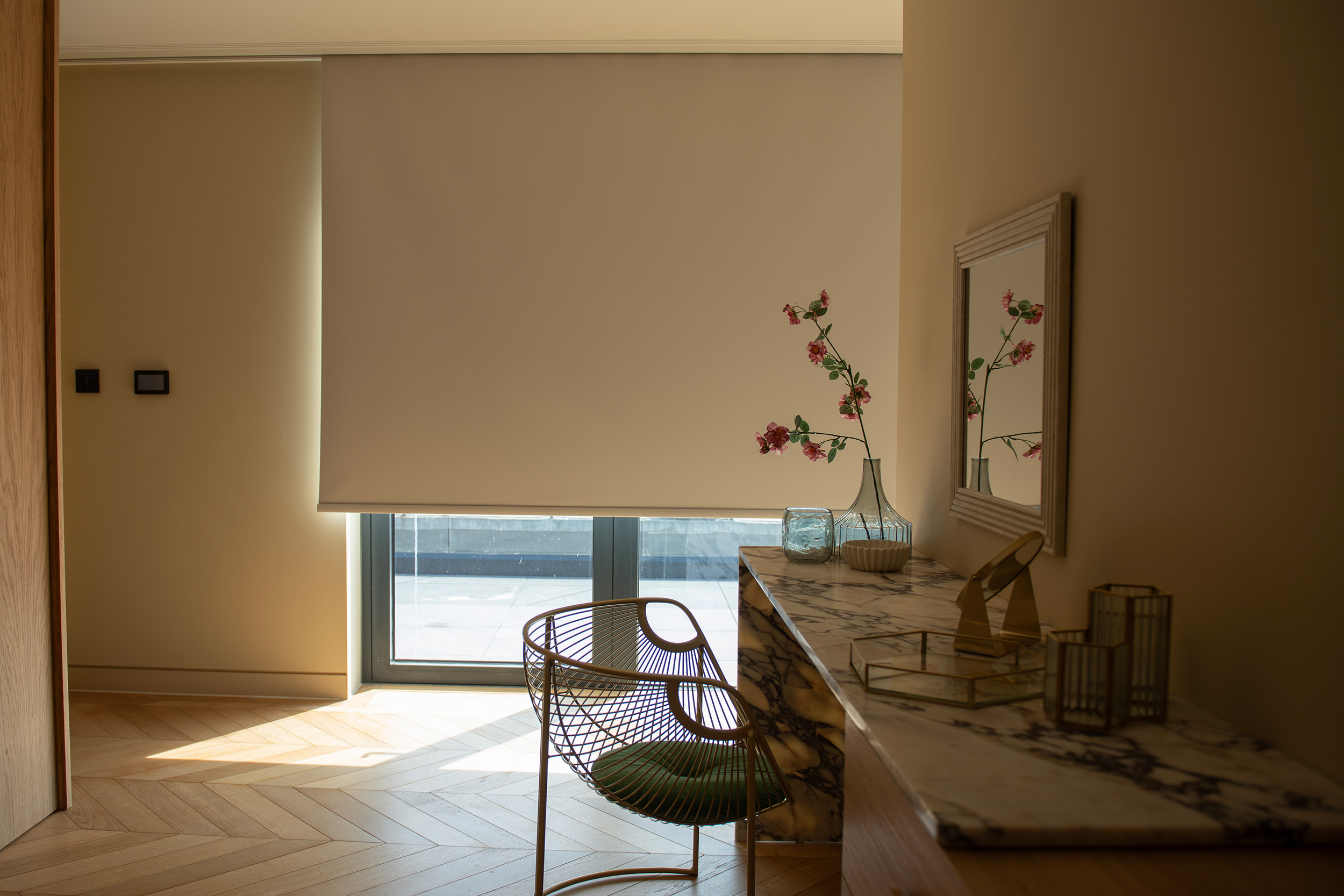 Decorquip cream roller blinds partially lowered over floor-to-ceiling windows in a neutral bedroom