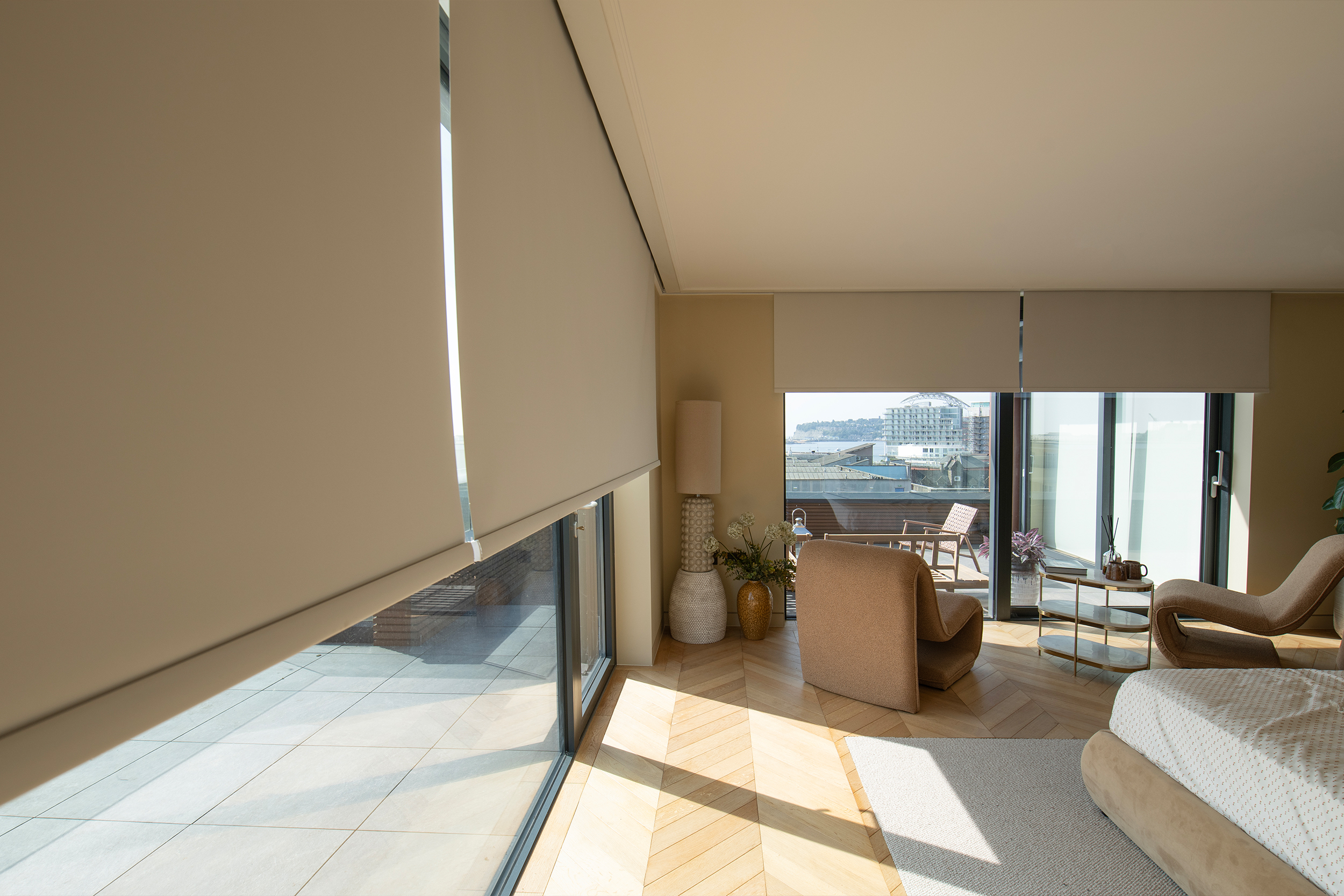 Decorquip cream roller blinds partially lowered over floor-to-ceiling windows in a neutral bedroom