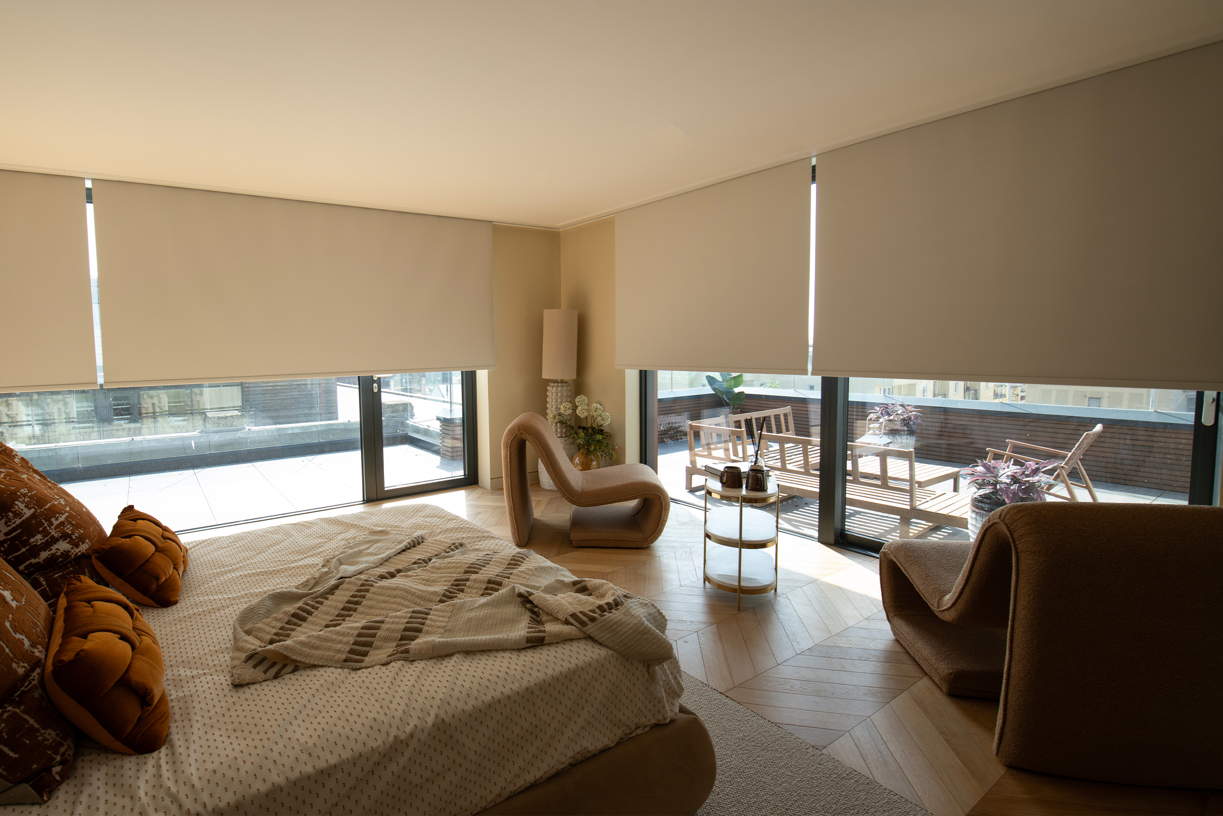 Decorquip cream roller blinds partially lowered over floor-to-ceiling windows in a neutral bedroom