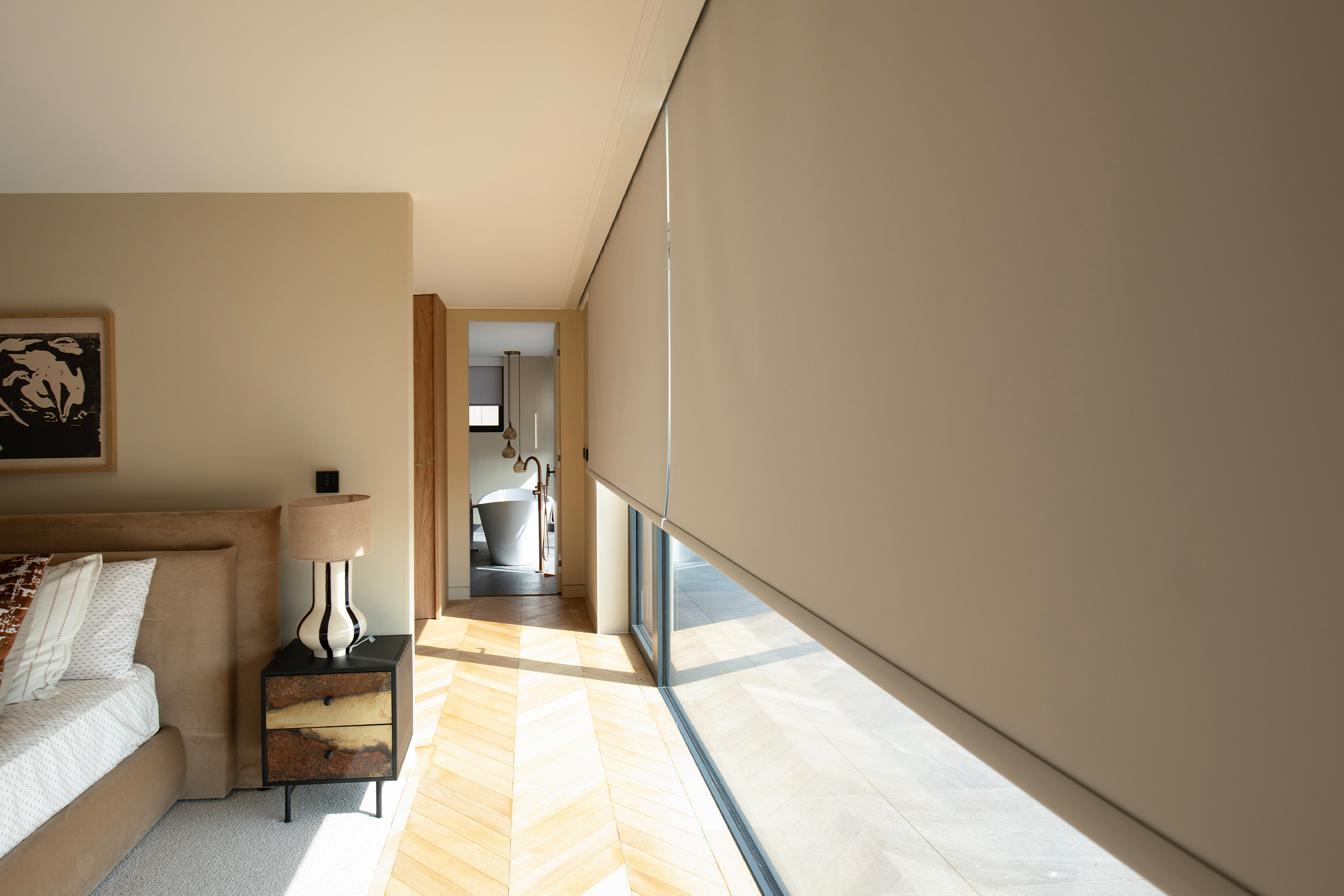 Decorquip cream roller blinds partially lowered over floor-to-ceiling windows in a neutral bedroom