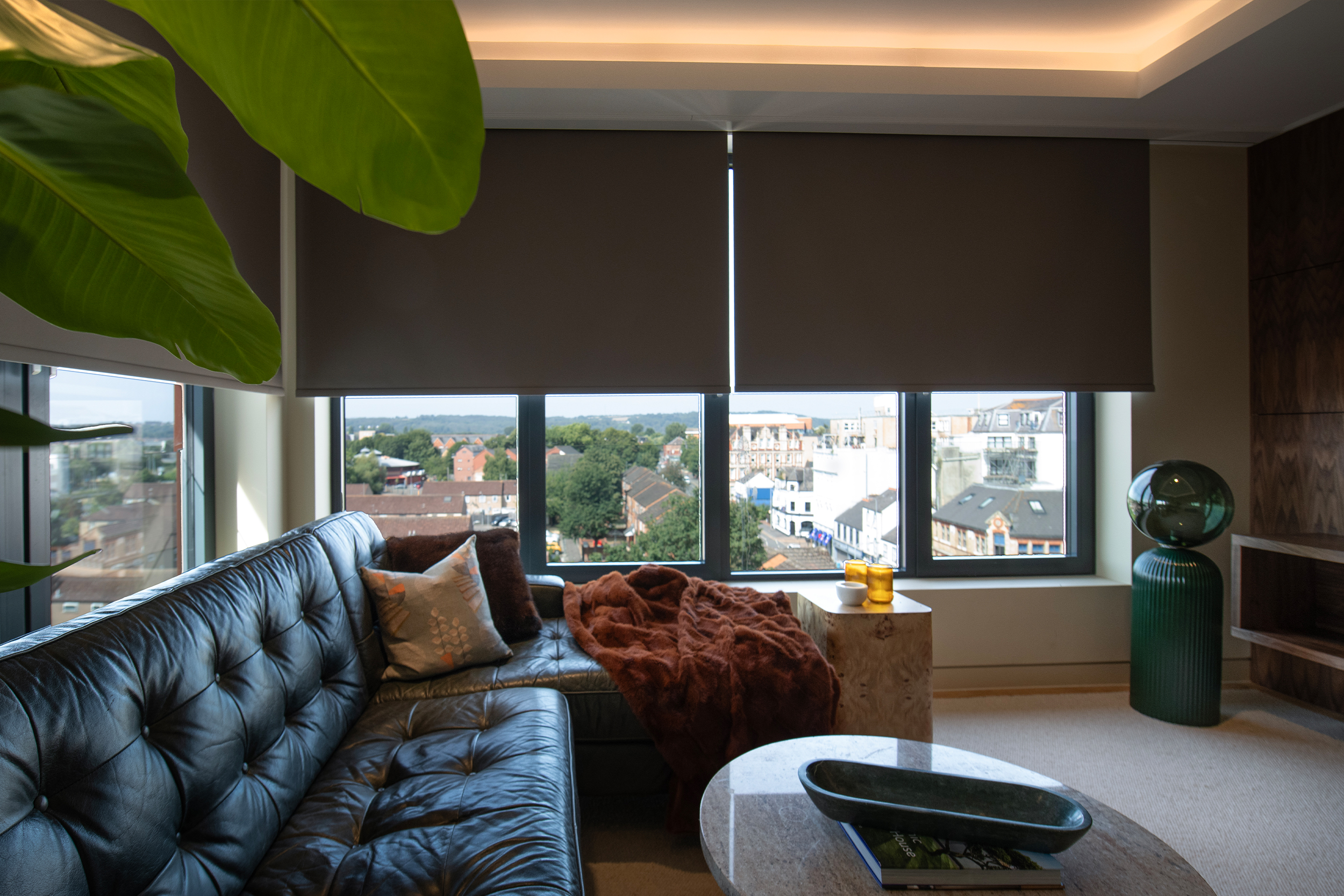 Decorquip dark brown roller blinds partially lowered over large windows in a modern living room