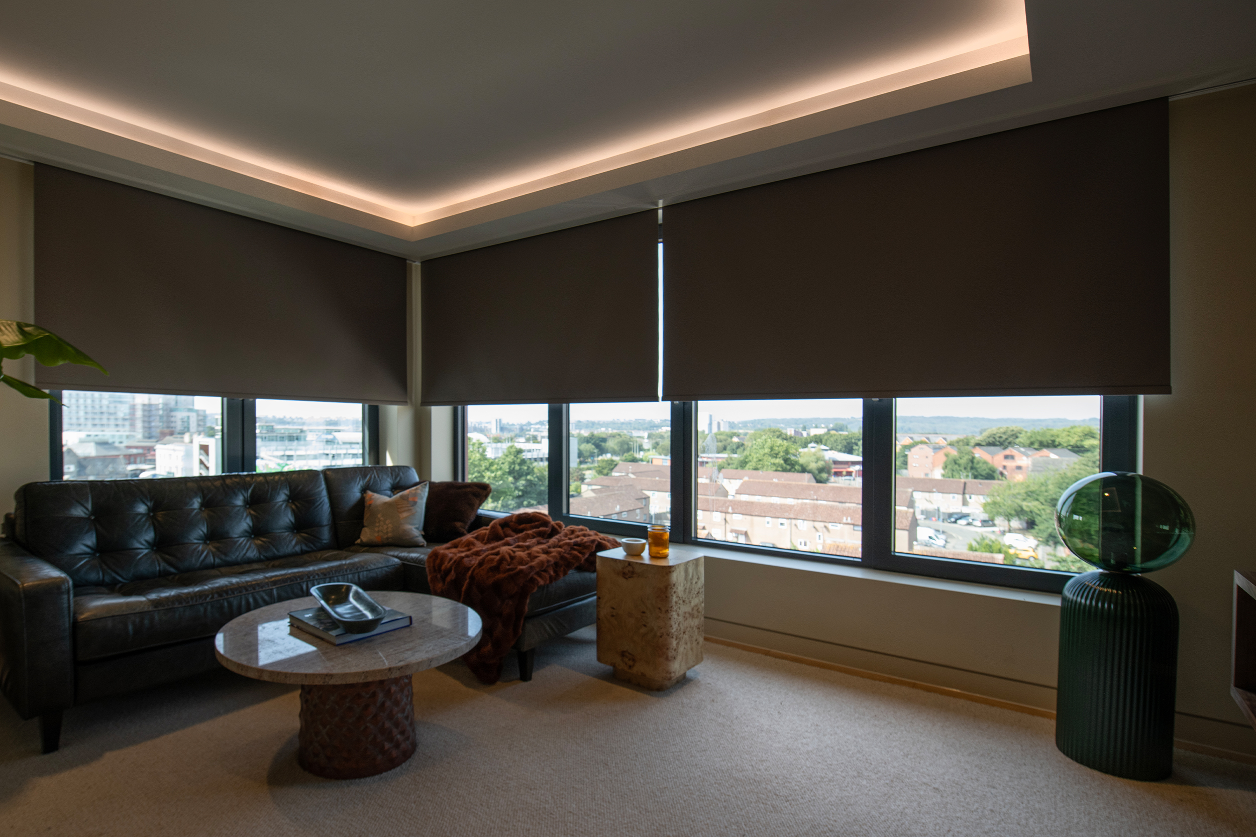 Decorquip dark brown roller blinds partially lowered over large windows in a modern living room