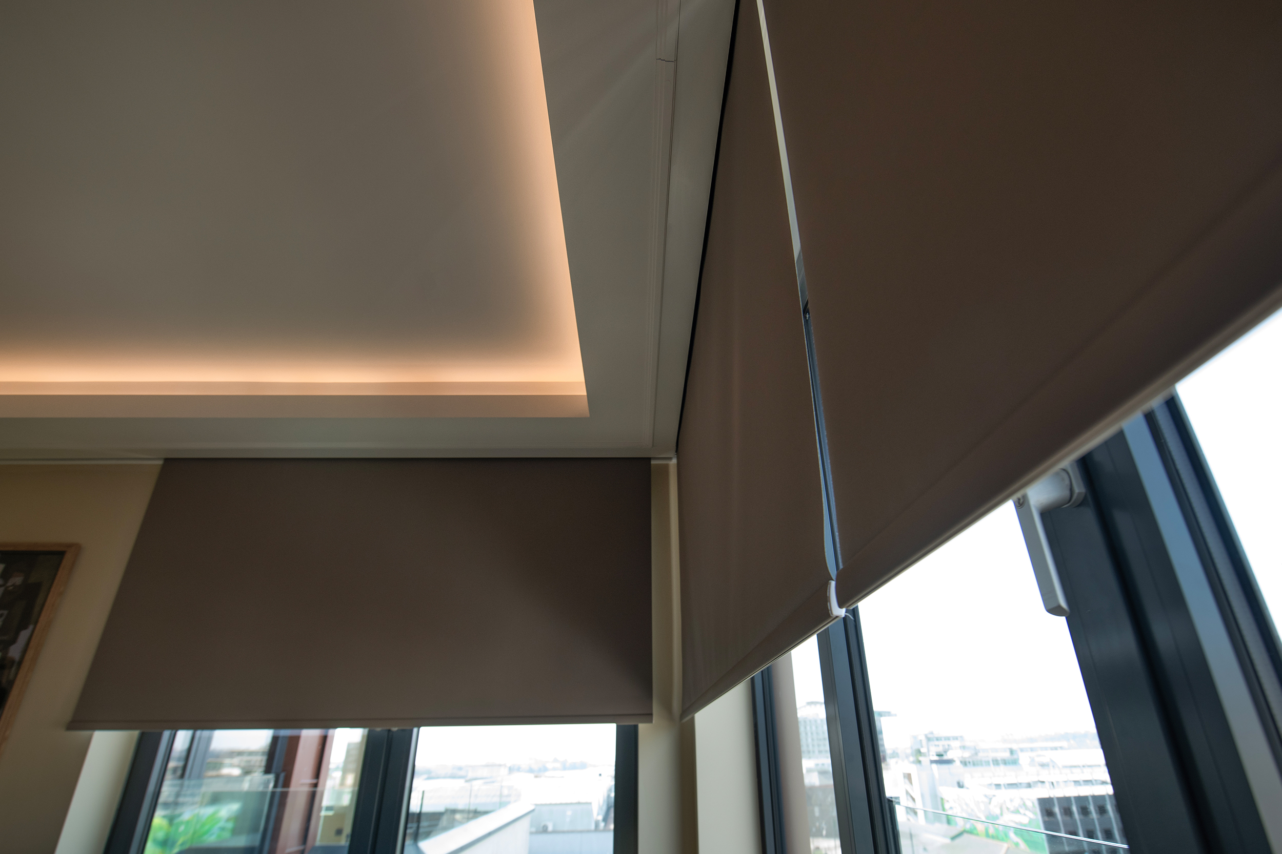 Decorquip dark brown roller blinds partially lowered over large windows in a modern living room