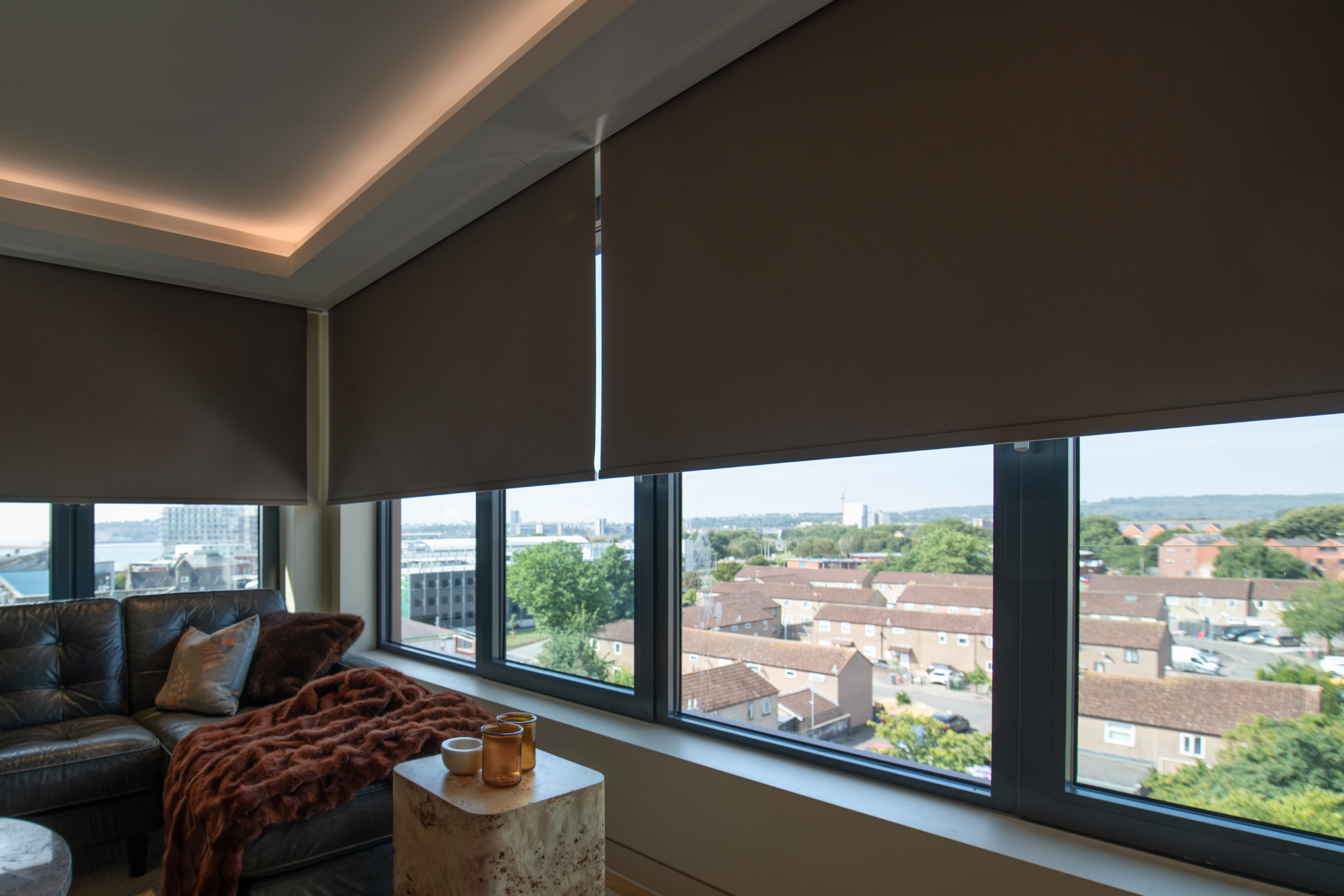 Decorquip dark brown roller blinds partially lowered over large windows in a modern living room