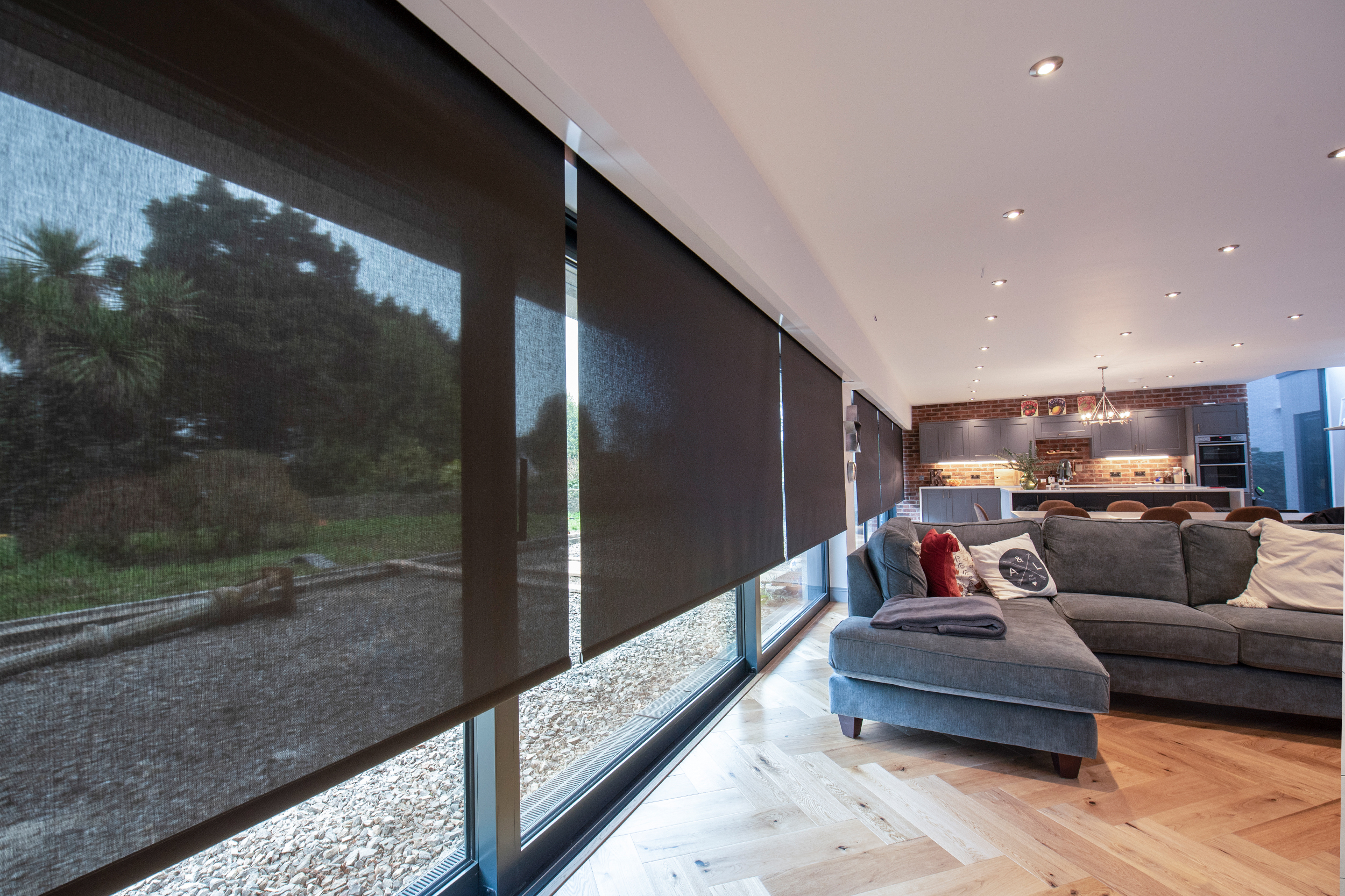 Decorquip black sheer roller blinds partially lowered across floor-to-ceiling windows in an open-plan living