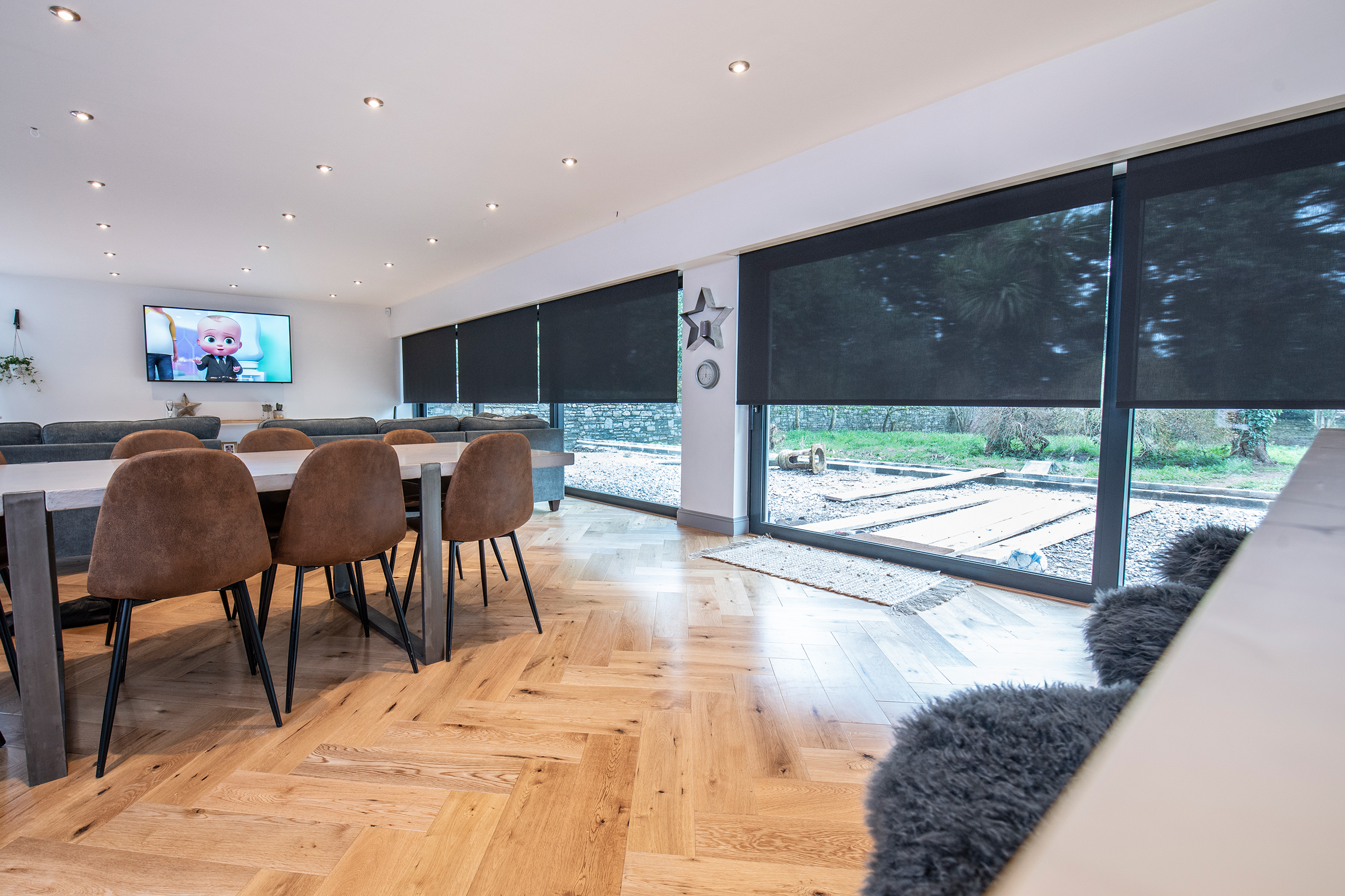 Decorquip black sheer roller blinds partially lowered across floor-to-ceiling windows in an open-plan living