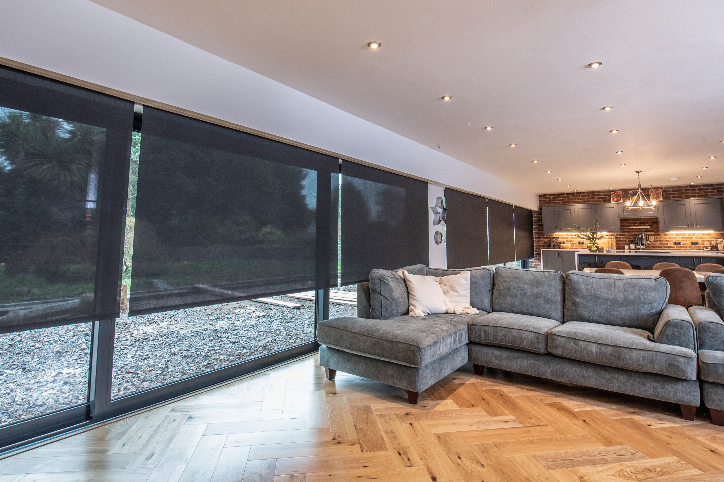 Decorquip black sheer roller blinds partially lowered across floor-to-ceiling windows in an open-plan living