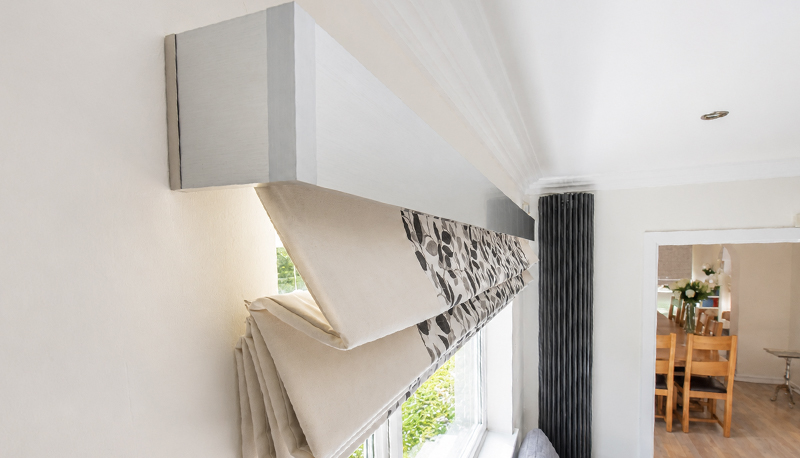 Decorquip patterned XL Roman blind partially raised beneath a brushed silver Capital Fascia in a living room